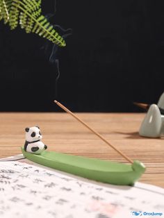 a toy panda bear sitting on top of a green toothbrush next to a plant