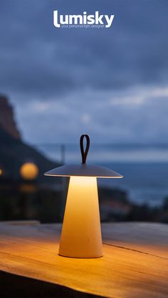 a lamp that is sitting on top of a wooden table in front of the ocean