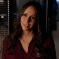 a woman with long hair wearing a red shirt and gold necklace smiling at the camera