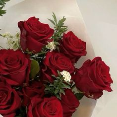 a bouquet of red roses sitting on top of a white tablecloth with greenery