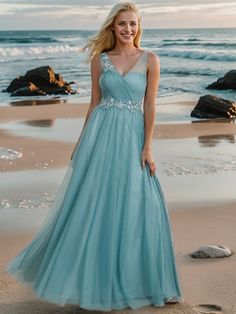 a woman standing on the beach wearing a blue dress with beaded waist and sleeves