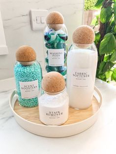 three bottles are sitting on a tray with soaps and bath salts in them next to some plants