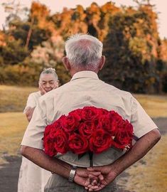 an older man holding a bouquet of red roses while standing next to another old man