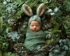 a baby wrapped up in a green blanket and wearing a knitted bunny ears hat