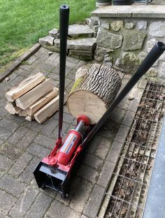 a red and black snow blower sitting on top of a brick walkway next to a pile of wood