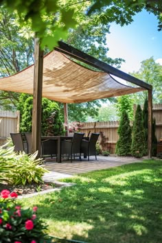 Outdoor patio with wicker chairs and a table under a shade canopy, surrounded by lush greenery and flowering plants. Fence and trees in the background. Shade Sails Backyard, Shade Sails For Deck, Shade Pergola Ideas, Backyard With Sunsail, Shade Ideas For Garden, Small Backyard Shade Ideas, Backyard Sail Shade Ideas, Backyard Sun Shade Ideas, Shade Sail Ideas Backyards