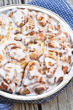 a pan filled with cinnamon rolls on top of a blue cloth next to a wooden table