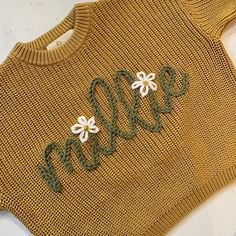 a knitted sweater with flowers and the word mom written in green yarn on it