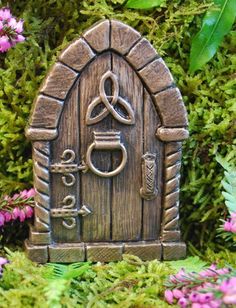 a small wooden door with a plant in front of it and flowers around the edges