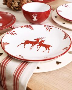 red and white plates with deer designs on them sitting on a wooden table next to pine cones