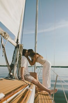 a man and woman sitting on the deck of a sailboat kissing each other,