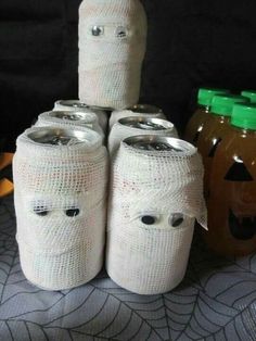 there are four jars wrapped in white paper with faces on them and two pumpkins behind them