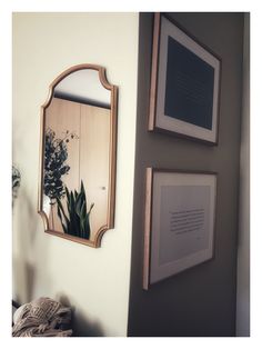 two framed pictures hang on the wall next to a mirror and plant in a vase