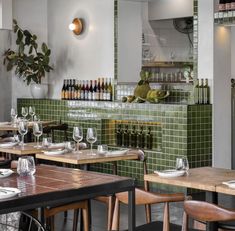 an empty restaurant with green tile walls and wooden tables, wine bottles on the wall