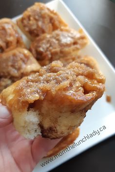 a hand is holding a piece of food on a white plate with cinnamon rolls in it