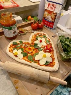 a heart shaped pizza sitting on top of a wooden cutting board next to vegetables and condiments