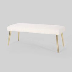 an upholstered bench with gold legs and a white fabric seat pad on top