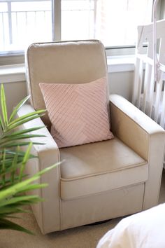 a chair with a pink pillow on it next to a bed and a potted plant