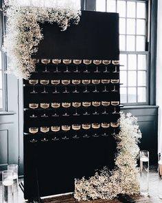 a tall black wall with lots of cups on it and flowers growing out of the top