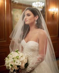 a woman in a wedding dress and veil holding a bouquet with white flowers on it