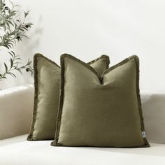 two green pillows sitting on top of a white couch next to a potted plant