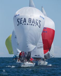 two sailboats in the ocean with sails down and one is red white and blue