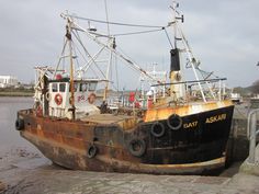 an old rusted fishing boat sitting on the shore in front of a body of water