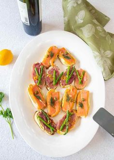 a white plate topped with sliced up sandwiches next to a bottle of wine and a knife