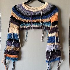 a multicolored knitted scarf hanging on a wall next to a pair of scissors