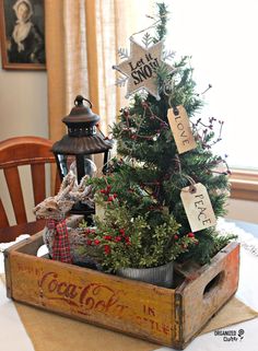 a small christmas tree in a wooden crate on top of a white tablecloth covered table