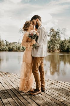 a bride and groom standing on a dock kissing