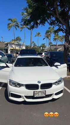 a white car parked in a parking lot next to some palm trees and other cars