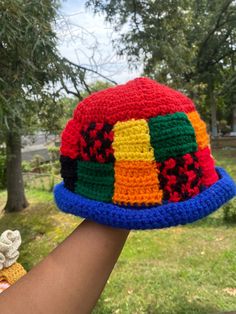 a hand holding a multicolored crocheted hat in front of a tree