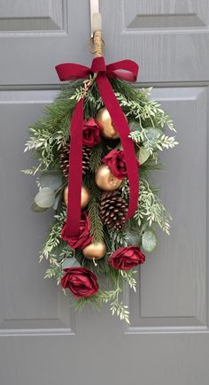 a wreath hanging on the front door with red roses and pine cones, greenery and bells