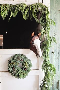 a horse head mounted to the side of a barn door with wreaths on it