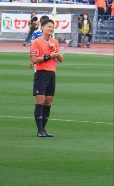 a man standing on top of a soccer field wearing black shorts and an orange shirt