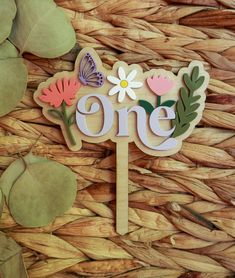 a cake topper with the word one on it next to some leaves and flowers