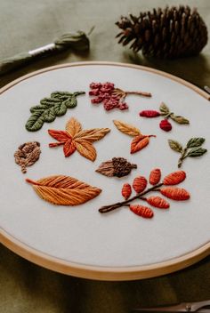 a close up of a embroidery on a table with a pine cone in the background