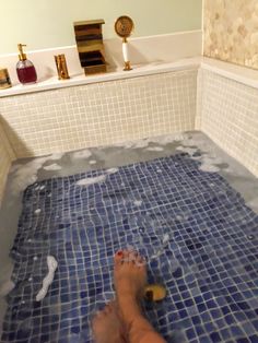 a person's feet in a bathtub with blue tiles on the floor and walls