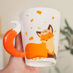 a hand holding a coffee cup with an orange fox design on the side and sprinkles around it