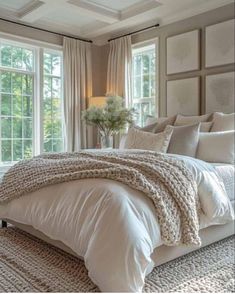 a large bed in a bedroom next to two windows with white curtains and pillows on them