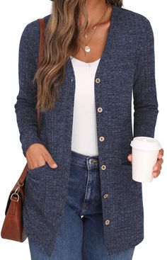 a woman wearing a blue cardigan sweater and jeans holding a coffee cup in her hand