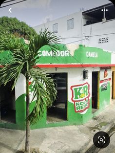 a green and white building with graffiti on it's side next to a palm tree