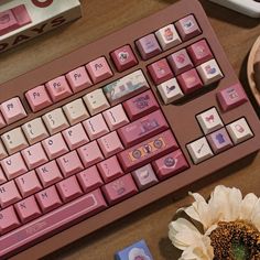 a pink keyboard sitting on top of a wooden desk next to a flower and other items