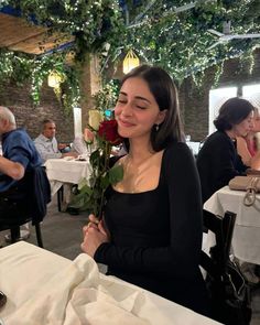 a woman sitting at a table with a rose in her hand and another person standing next to her