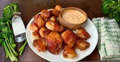 a plate with bacon and broccoli on it next to a bowl of dip