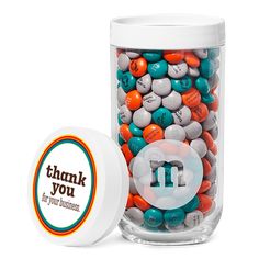 a jar filled with lots of colorful candies on top of a white table next to a container that says thank you