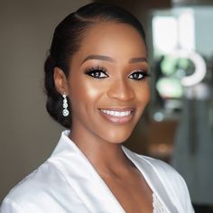 a woman in a white dress smiling at the camera with her hair pulled back and wearing earrings