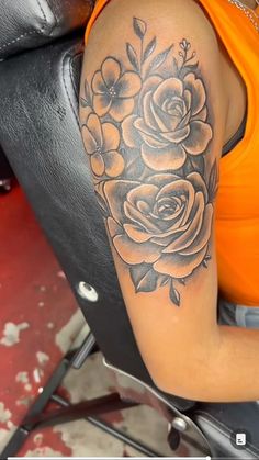 a woman is sitting in a chair with a tattoo on her arm and flowers behind her