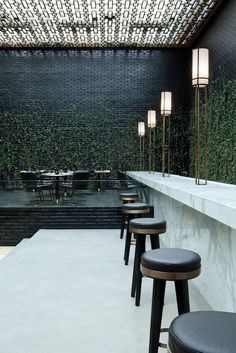 several stools are lined up in front of an outdoor bar with greenery on the wall